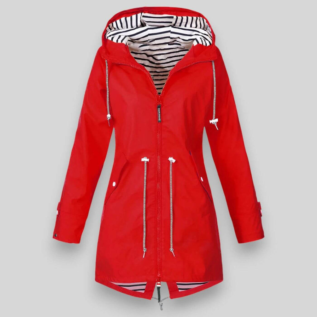 Noa™ waterproof jacket by Les Odettes, sleek coat with a hood, shown in a modern outdoor setting with urban architecture.