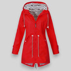 Noa™ waterproof jacket by Les Odettes, sleek coat with a hood, shown in a modern outdoor setting with urban architecture.