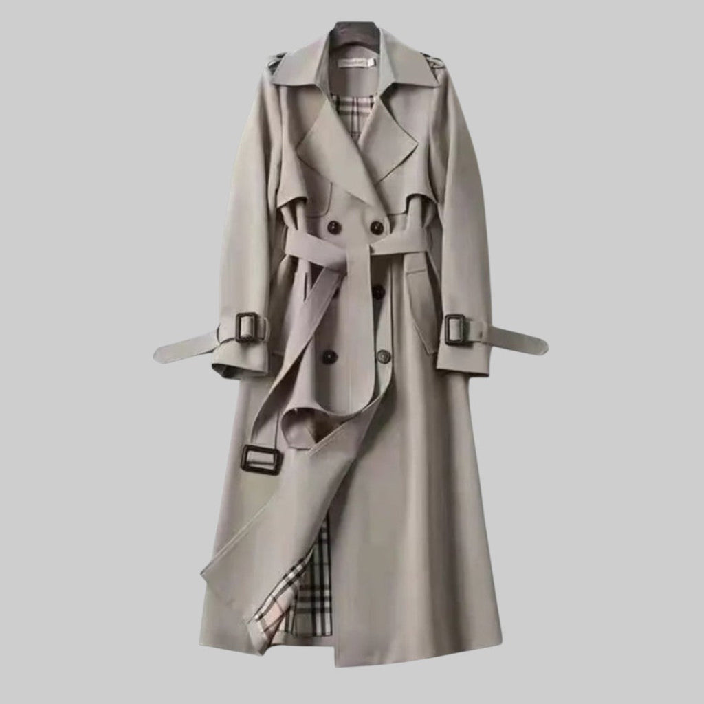 Les Odettes Aleah™ classic trench coat in beige fabric, featuring a double-breasted design and belted waist, displayed on a hanger.