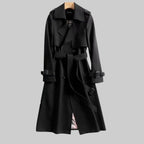 Les Odettes Aleah™ classic trench coat in beige, shown hanging on a wooden hanger with a belt and double-breasted design.